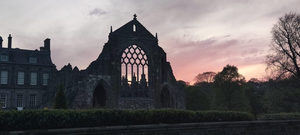 Dark silhouette of Holyrood Abbey set against a vibrant, dimly lit sunset sky.